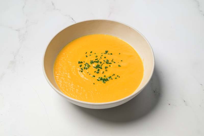 A white bowl filled with creamy carrot and ginger soup.