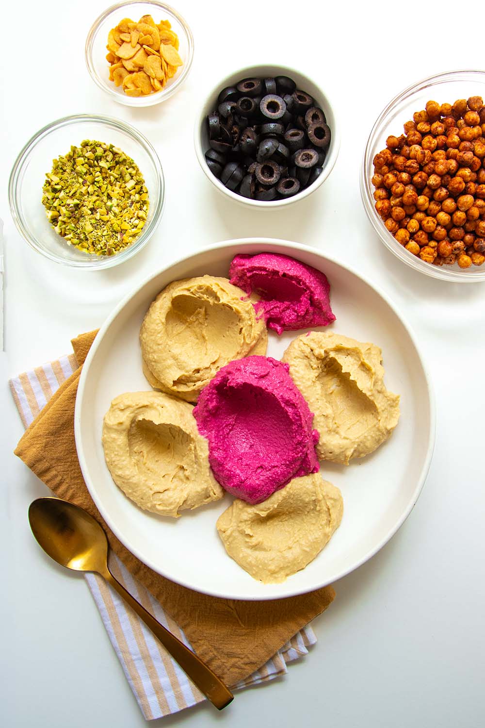 Building a hummus platter, the first few scoops of hummus in varying colors of plain, traditional hummus, and bright magenta beet hummus.
